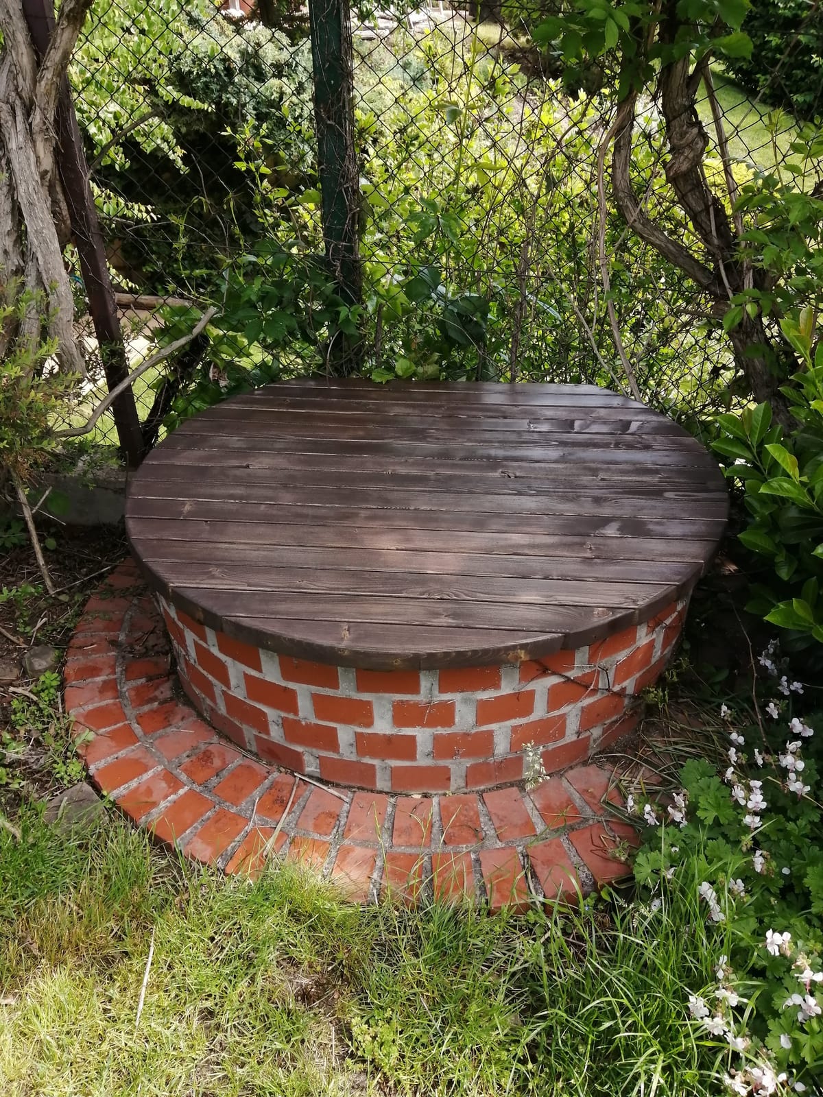 Kulatý tmavě mořený dřevěný poklop na cihlové studni v zahradě