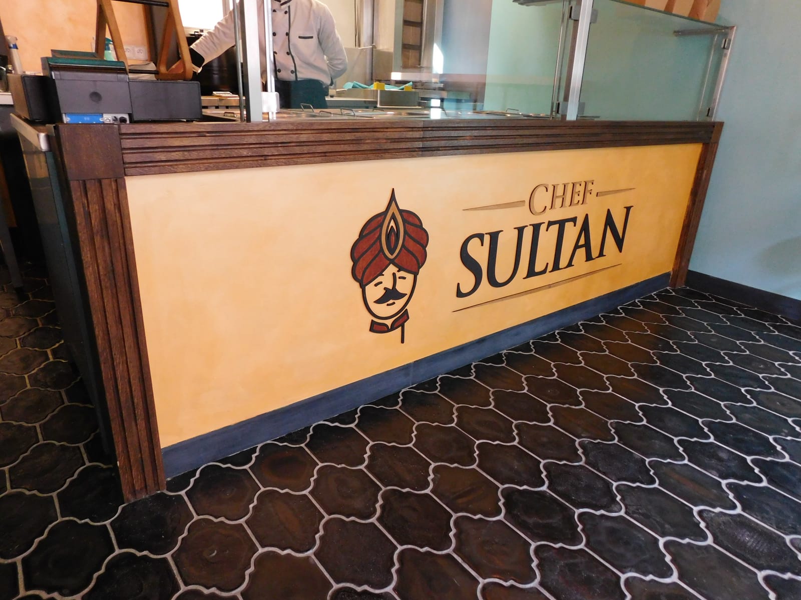 Výdejní pult restaurace Chef Sultan s tmavým dubovým rámem a vyřezávaným logem